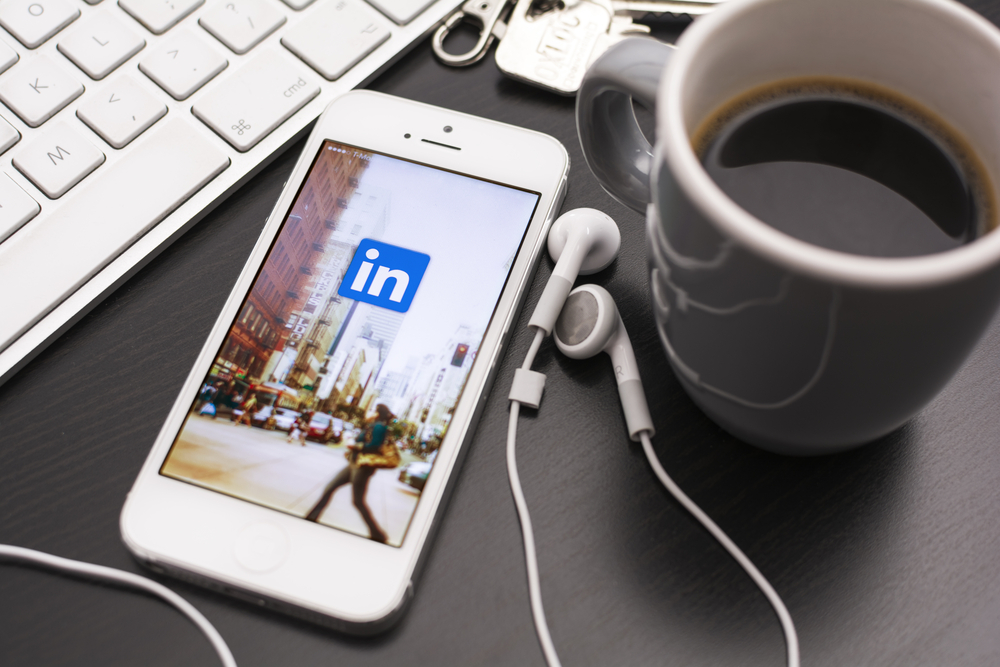 LinkedIn on iPhone with a cup of black coffee next to a computer keyboard
